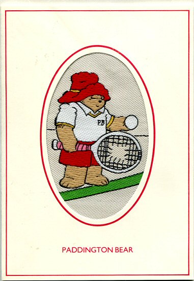 J & J Cash woven card, with title words only: Paddington Bear, but woven image of Paddington holding a tennis ball and racket with a hole in the strings